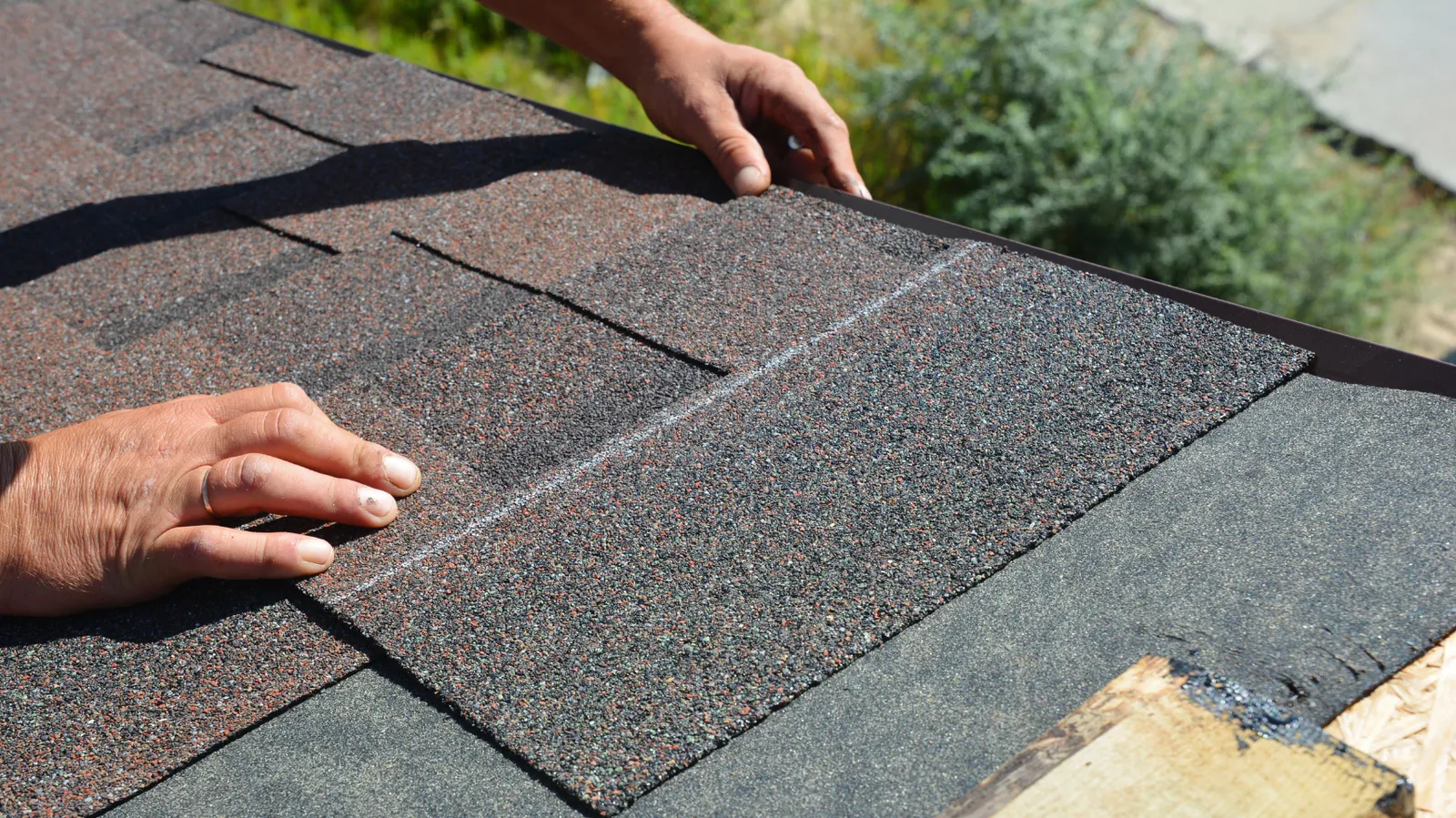 Asphalt shingle courses being laid at a roof edge by a roofer's hands