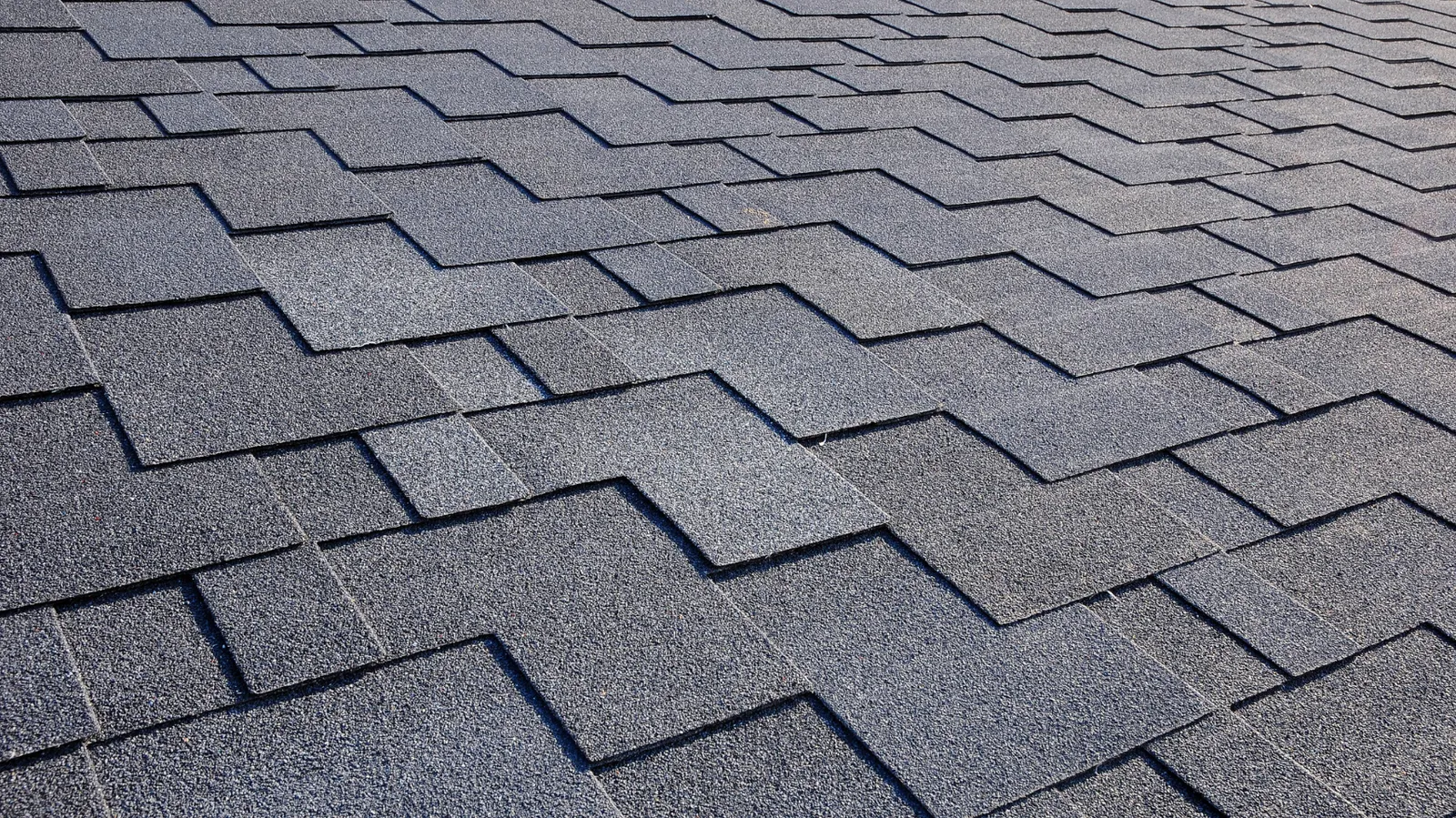 Close view of dark gray asphalt shingles in a staggered pattern