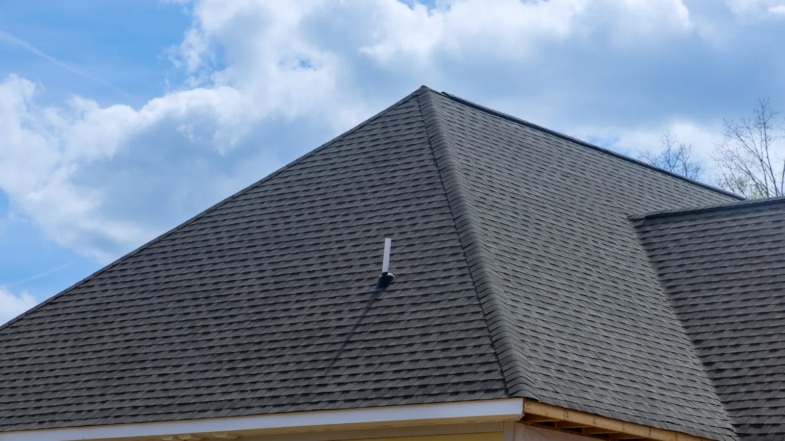 Dark shingle hip roof with a vent pipe under cloudy sky