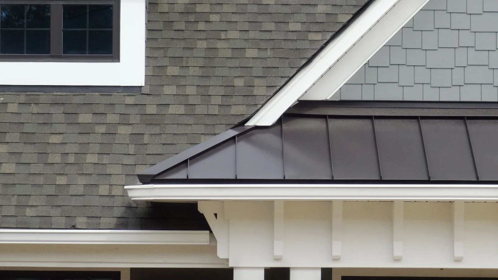 Dark standing seam roof with white trim meeting a gray shingle roof