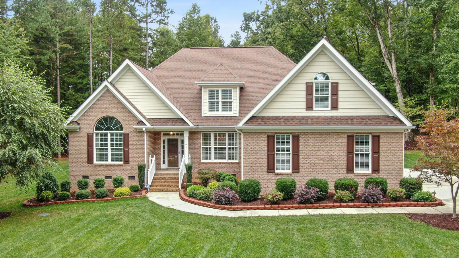 Brick home featuring an arched window beneath a brown architectural shingle roof