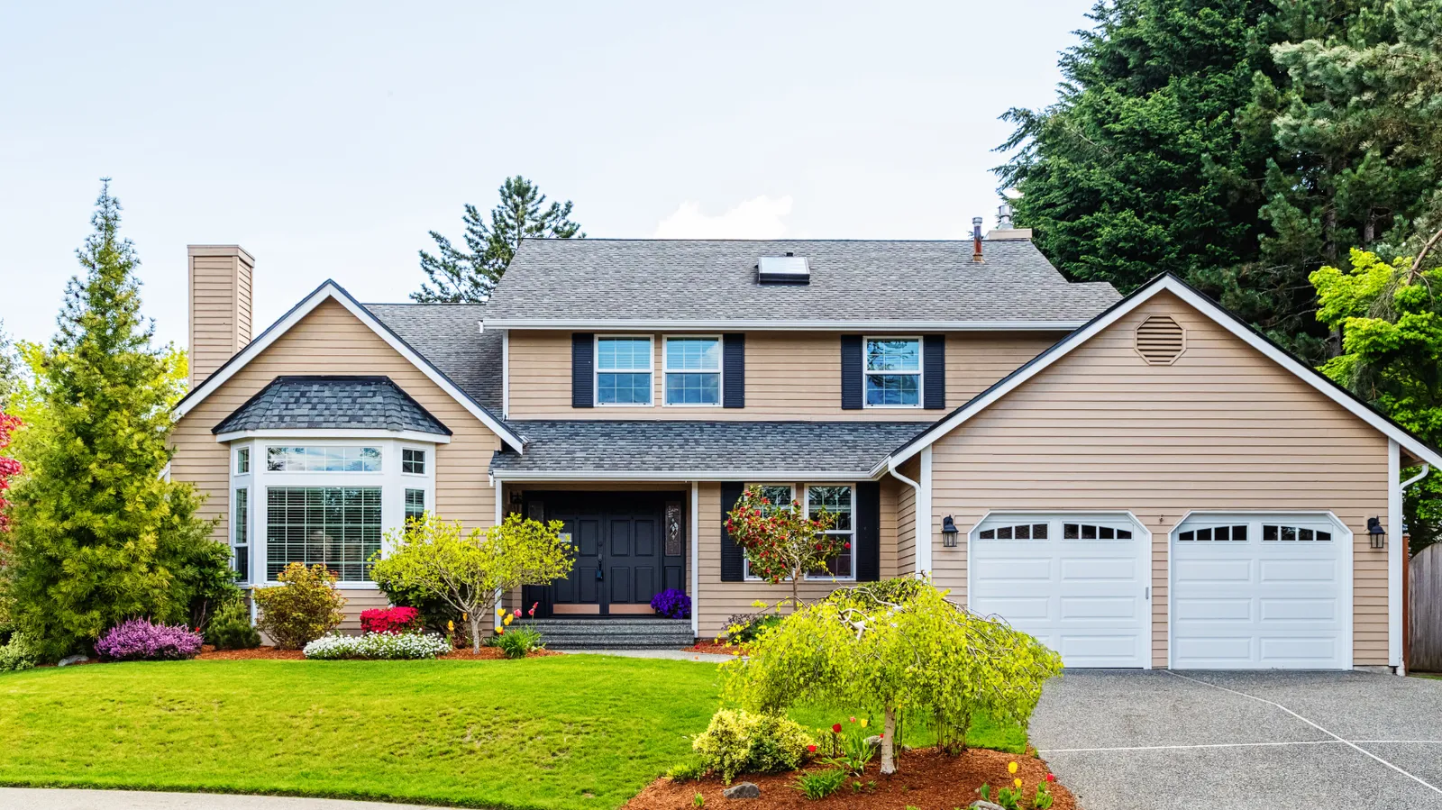 Gray asphalt shingle roof on a beige two-story home with black shutters