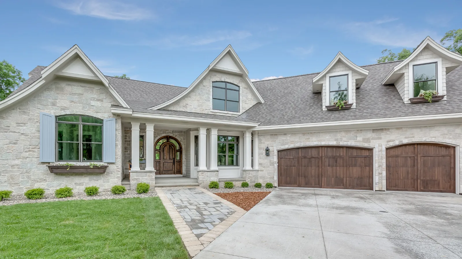 Blue shuttered light stone home beneath a gray architectural shingle roof