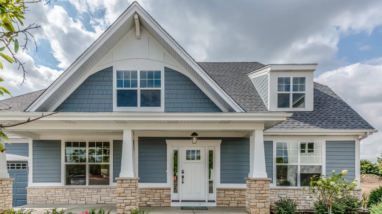 Gray shingle roof and stone porch columns on a blue craftsman home