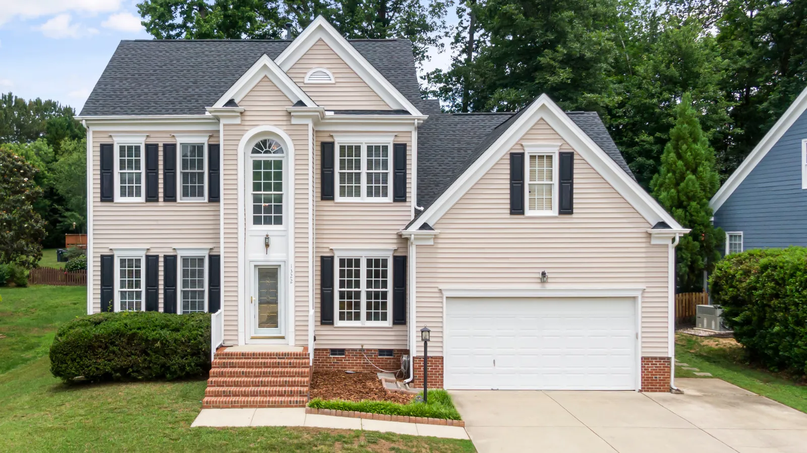 Beige two-story home with dark shingle roof and black shutters