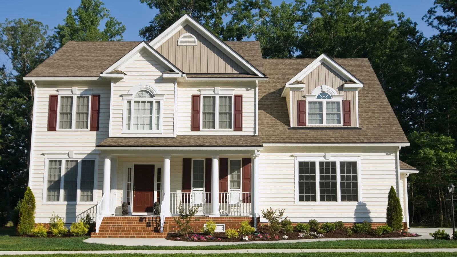 Cream two-story house with brown shingle roof and covered porch