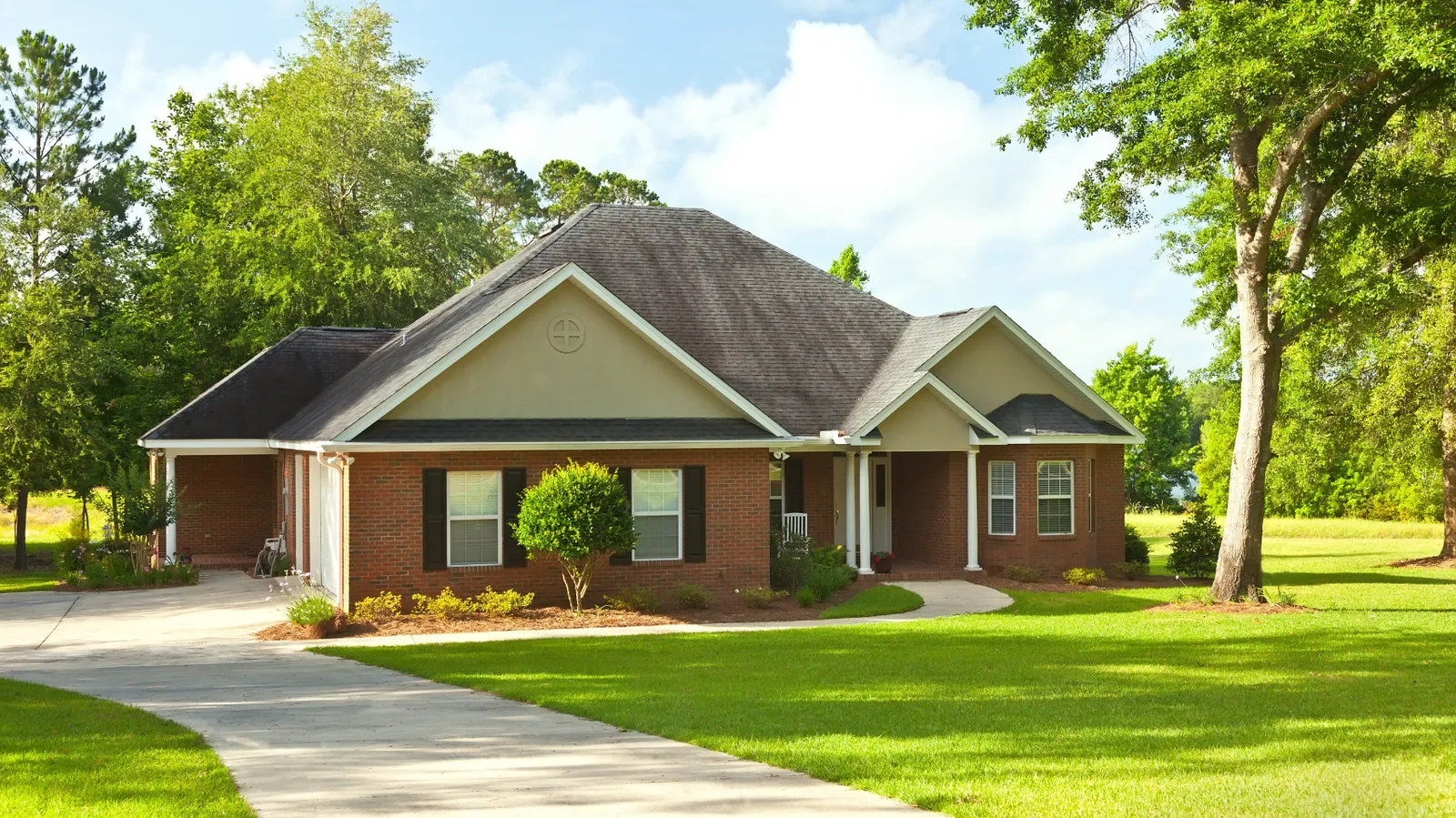 Brick ranch home with gray shingle roof shaded by mature trees