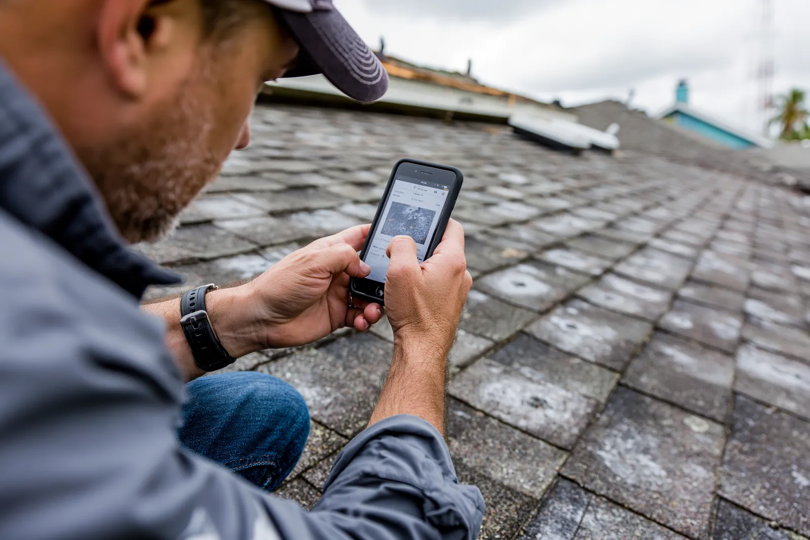 Using a smartphone a roofer photographs a weathered shingle roof