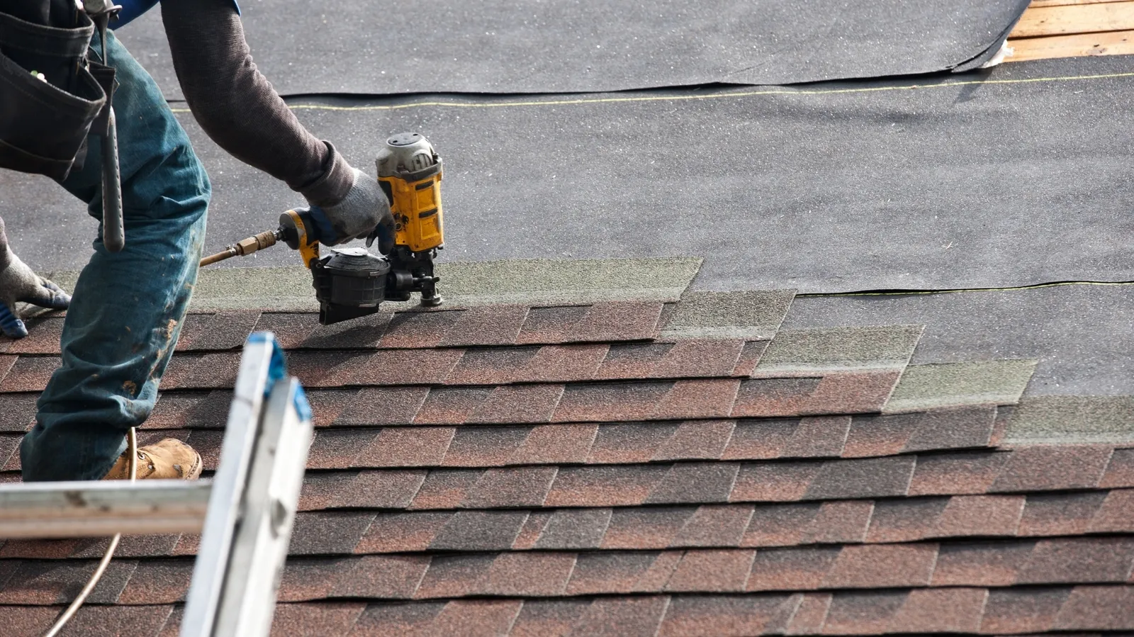 Pneumatic coil nailer in a roofer's hands fastening asphalt shingles