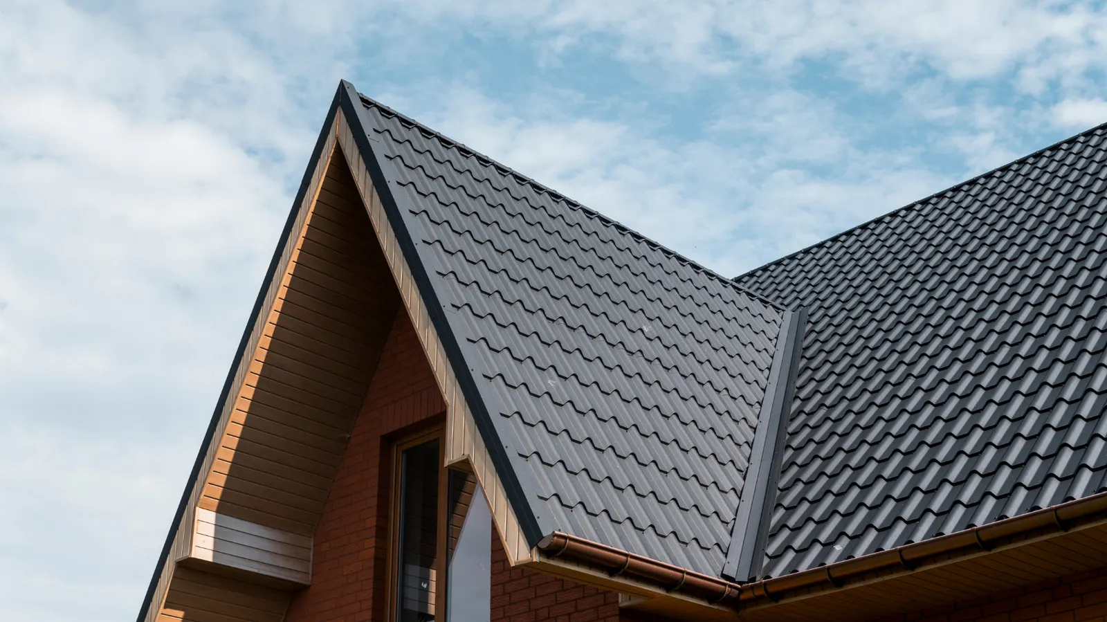 Dark metal roof tiles on a steep gable above a brick wall