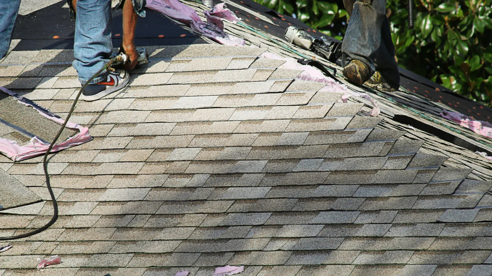 Nail gun used by a roofer on light brown shingles near the ridge